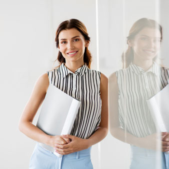 Mujer con blusa de rayas sosteniendo una carpeta blanca junto a una pared de cristal